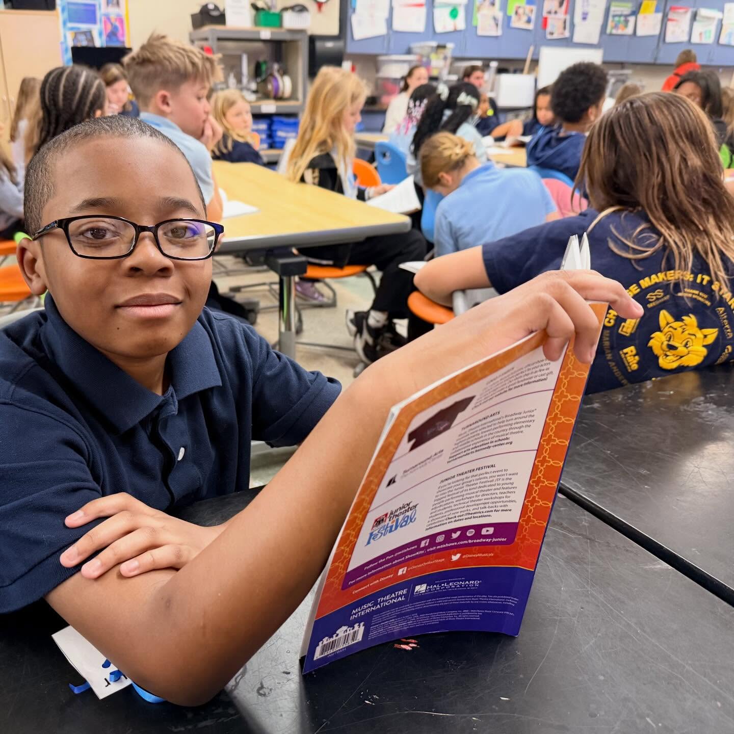 Marian Anderson Students Engaged in Classroom Learning Student reading a book at a classroom table while classmates work together in the background.